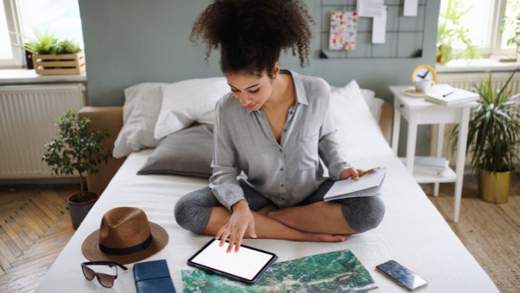 woman sitting on bed surrounded by trip planning tools