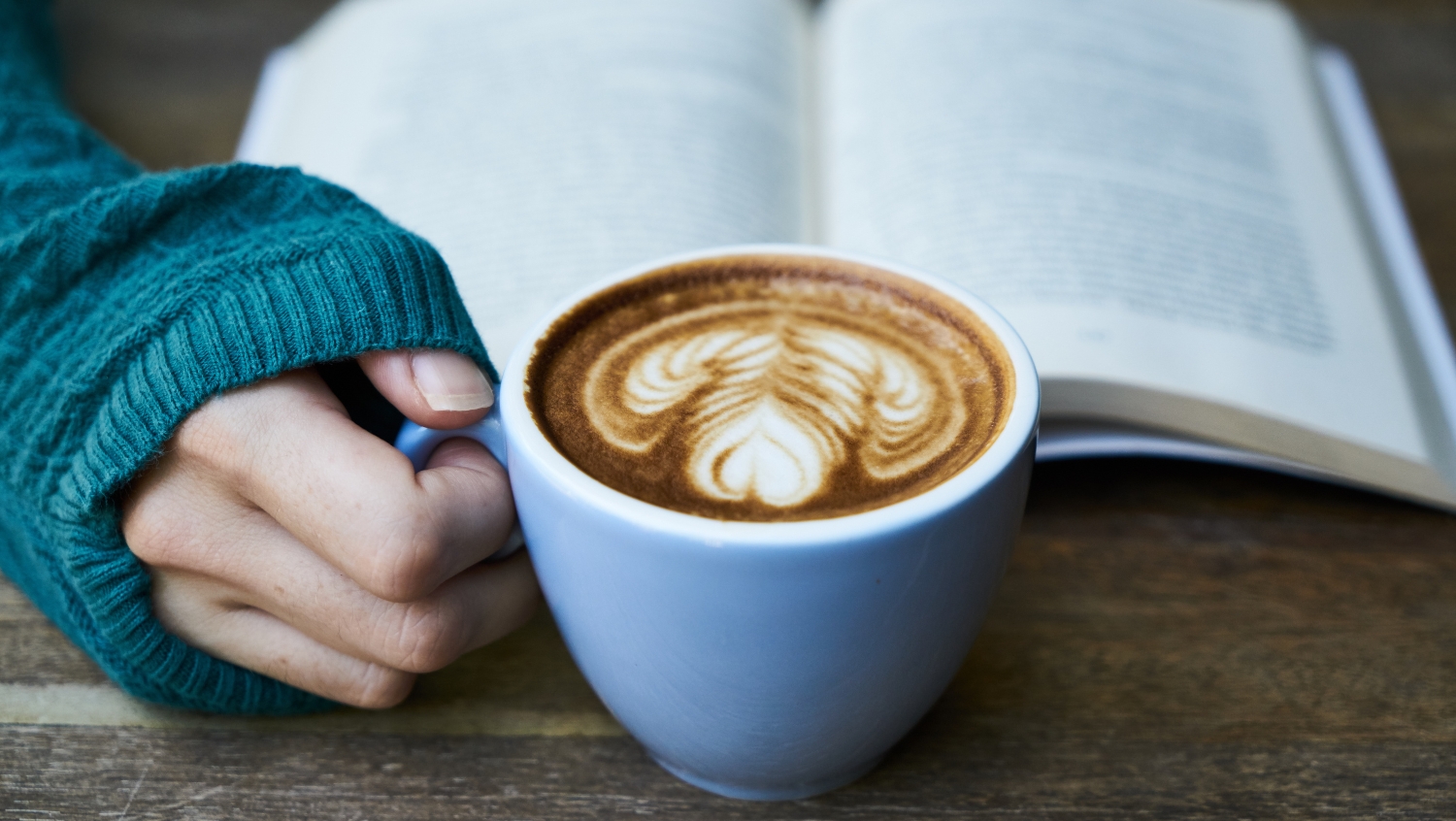 hand holding a mug of coffee, book of poems about travel open