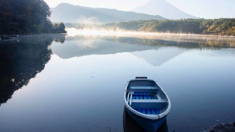 A solo point of view of a rowboat on a lake near Mount Fuji.